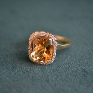 Pode incluir: Um anel de ouro com uma grande pedra de top&aacute;zio de forma quadrada cercada por um halo de diamantes menores.