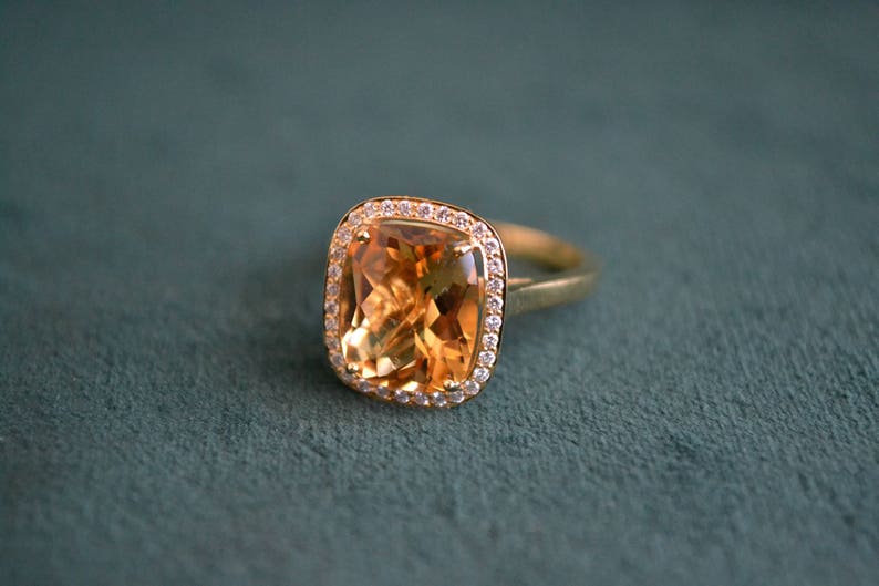 Pode incluir: Um anel de ouro com uma grande pedra de top&aacute;zio de forma quadrada cercada por um halo de diamantes menores.
