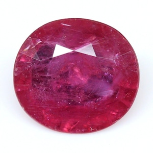 May include: A vibrant, oval-cut ruby gemstone featuring a deep magenta-red hue. The stone displays a faceted surface with visible internal inclusions and natural crystalline structures, reflecting light across its polished, translucent top surface.