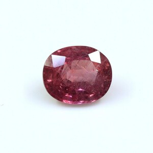 May include: An oval-cut gemstone in a rich pink shade. The gem's surface is multi-faceted, catching and reflecting light. The stone is presented on a plain white backdrop, emphasizing its colour and the way it catches the light.