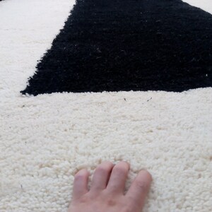 May include: A white and black shag rug with a hand resting on the white portion of the rug.