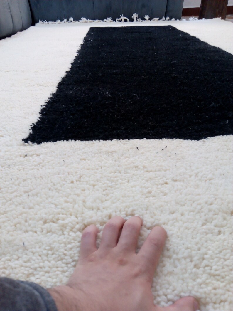 May include: A white and black shag rug with a hand resting on the white portion of the rug.