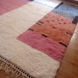 May include: A white, pink, and orange geometric patterned rug with black accents and fringe on the edges.