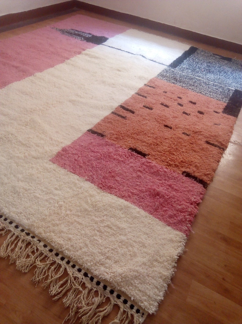 May include: A white, pink, and orange geometric patterned rug with black accents and fringe on the edges.