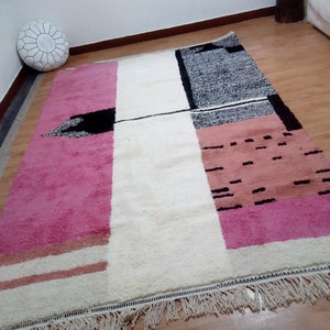 May include: A white, pink, and black geometric patterned rug with fringe. The rug has a modern design with abstract shapes and lines.