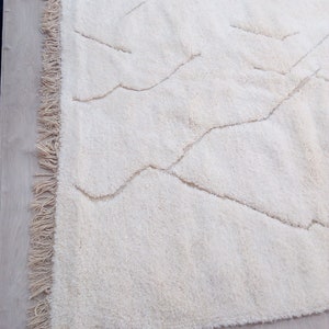 Puede incluir: Una alfombra blanca de pelo largo con un patr&oacute;n ondulado. La alfombra tiene un borde de flecos.