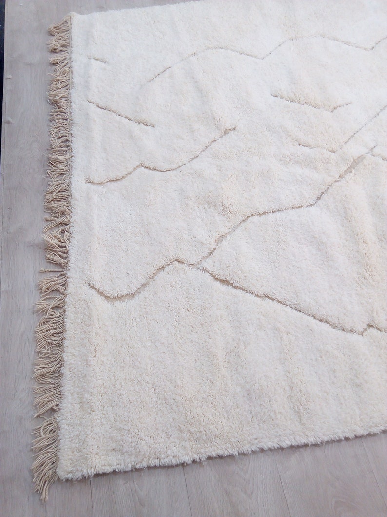 Puede incluir: Una alfombra blanca de pelo largo con un patr&oacute;n ondulado. La alfombra tiene un borde de flecos.