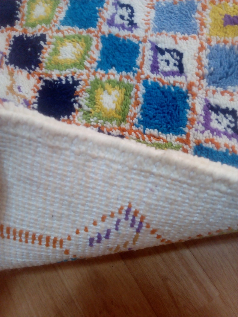 May include: A colorful, geometric patterned rug with a white fringe. The rug is made of a soft, fluffy material and has a variety of colors, including blue, green, yellow, orange, and purple.