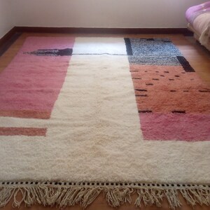 May include: A white, pink, and orange geometric patterned rug with a black fringe border. The rug has a white center with pink and orange sections on either side.