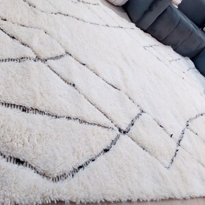 May include: A white shag rug with a geometric pattern of black lines. The rug has a soft, fluffy texture.