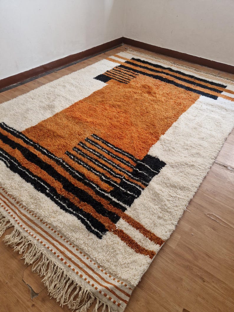 May include: A white and orange geometric patterned rug with black accents and fringe on the edges.