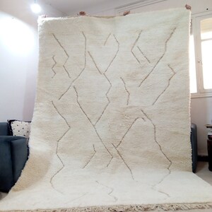 Puede incluir: Una alfombra marroqu&iacute; blanca con un patr&oacute;n geom&eacute;trico en un tono de blanco m&aacute;s claro. La alfombra tiene un borde de flecos.