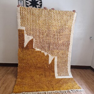 May include: A large, hand-woven rug with a geometric pattern in shades of yellow and white. The rug has a thick, fluffy pile and a fringe border.