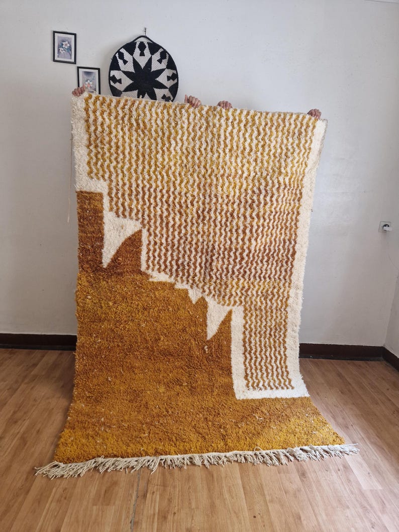 May include: A large, hand-woven rug with a geometric pattern in shades of yellow and white. The rug has a thick, fluffy pile and a fringe border.