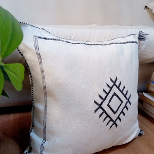 May include: White throw pillow with a black geometric design. The pillow has a black border and tassels.