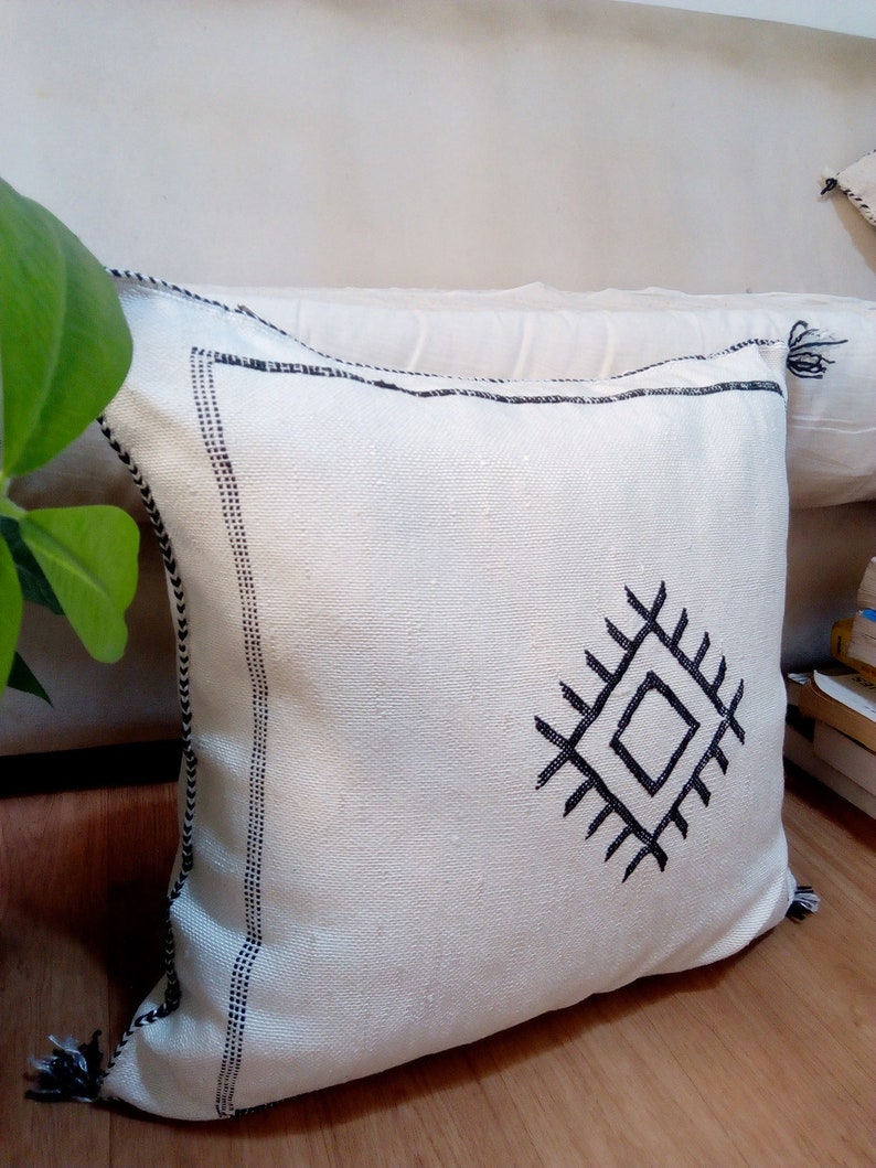 May include: White throw pillow with a black geometric design. The pillow has a black border and tassels.