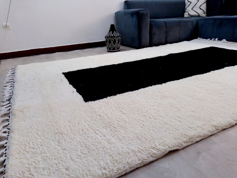 May include: A white shag rug with a black rectangular stripe in the center. The rug has fringe on the edges.