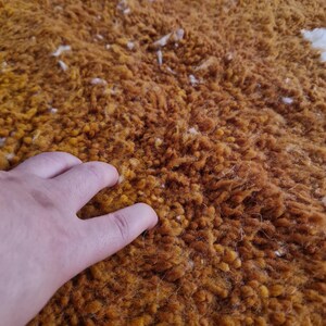 May include: Close-up of a soft, fluffy rug with a deep orange color and white flecks throughout. The rug has a textured, almost shag-like appearance.