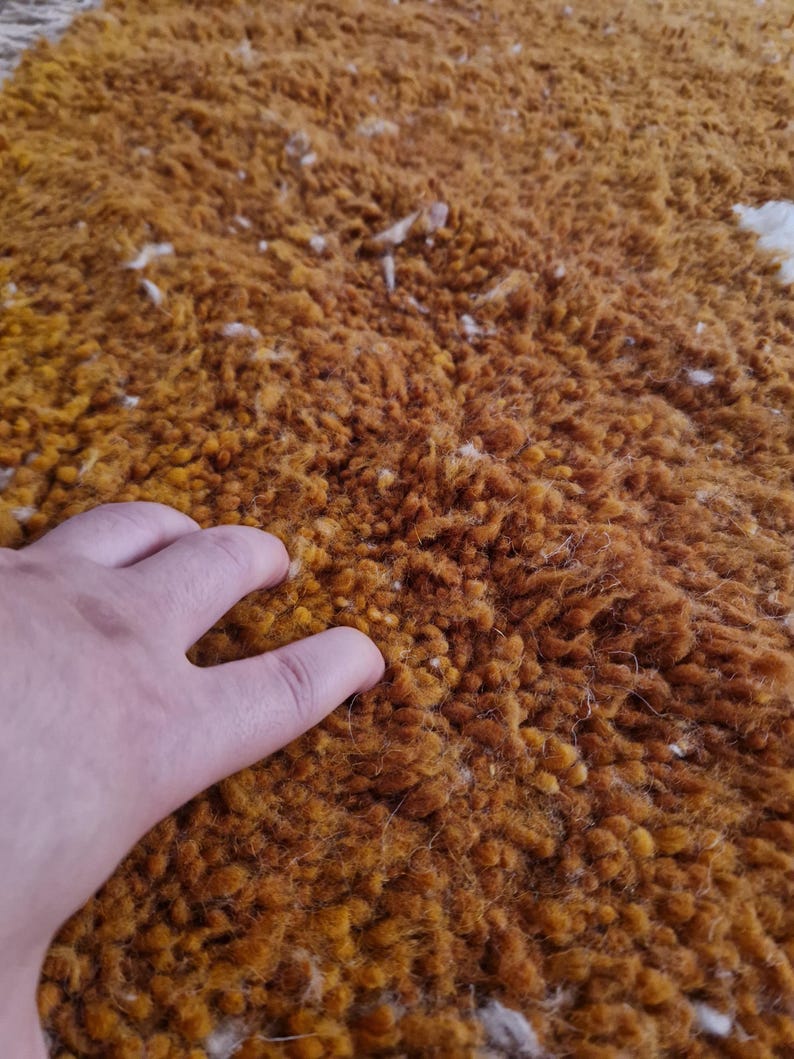 May include: Close-up of a soft, fluffy rug with a deep orange color and white flecks throughout. The rug has a textured, almost shag-like appearance.