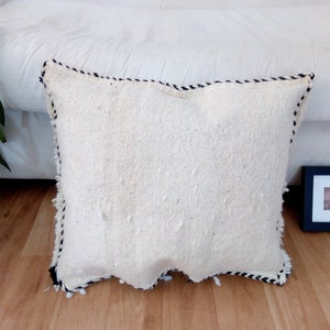 May include: White throw pillow with a black and white trim. The pillow is made of a soft, textured fabric and has a slightly frayed edge.