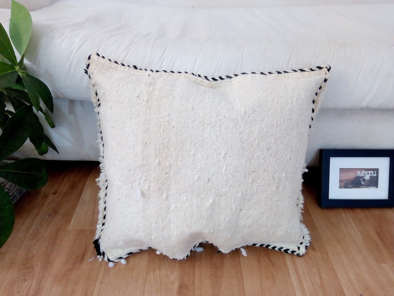 May include: White throw pillow with a black and white trim. The pillow is made of a soft, textured fabric and has a slightly frayed edge.