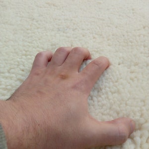 Puede incluir: Primer plano de una mano tocando una alfombra blanca y esponjosa. La alfombra tiene una textura suave y mullida.