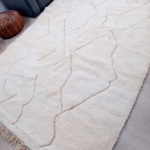 Puede incluir: Una alfombra de pelo blanco con un patr&oacute;n geom&eacute;trico en un tono de blanco m&aacute;s claro. La alfombra tiene un borde de flecos.