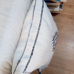 May include: White throw pillow with black geometric embroidery and black tassels. The pillow has a white background with black stitching around the edges.