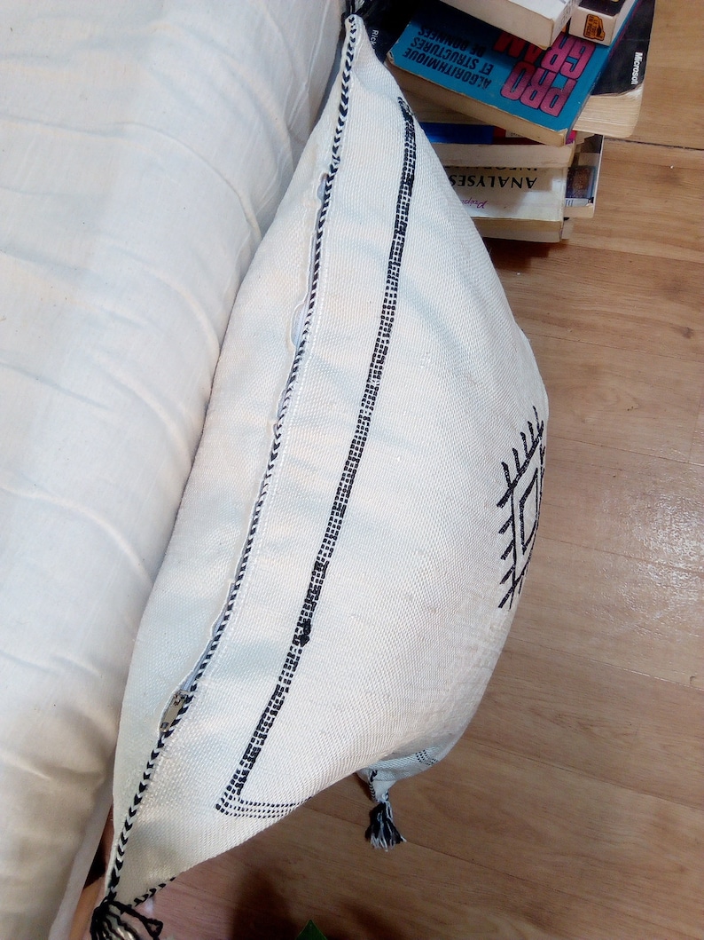 May include: White throw pillow with black geometric embroidery and black tassels. The pillow has a white background with black stitching around the edges.