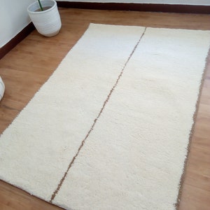 Puede incluir: Una alfombra de pelo blanco con una franja marr&oacute;n en el centro. La alfombra est&aacute; sobre un suelo de madera.