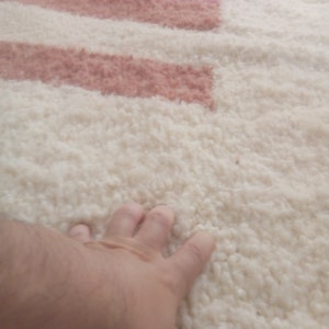 May include: A close-up of a white fluffy rug with pink and peach stripes. A hand is resting on the rug.