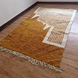 May include: A mustard yellow and white geometric patterned rug with fringe. The rug has a modern design with a white geometric pattern on a mustard yellow background.