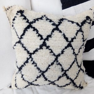 Puede incluir: Cojín de decoración blanco y negro con textura esponjosa. El cojín tiene un patrón de diamante con líneas negras.