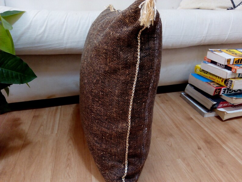 Puede incluir: Una almohada rectangular marr&oacute;n y beige con flecos blancos. La almohada est&aacute; hecha de una tela texturizada y tiene una costura blanca en el lateral.
