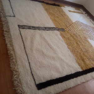 Puede incluir: Una alfombra blanca y beige con dise&ntilde;os geom&eacute;tricos negros. La alfombra tiene un borde de flecos.