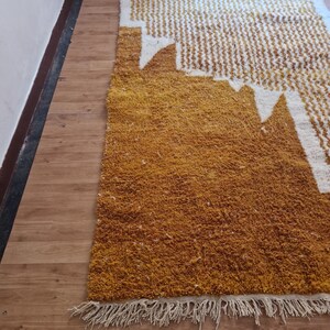 May include: A mustard yellow and white patterned rug with a fringe border. The rug has a geometric design with white shapes on a yellow background.