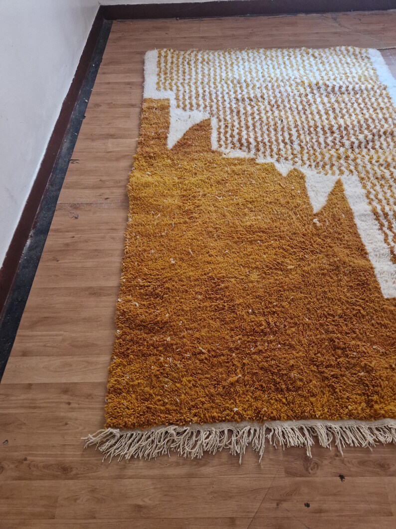 May include: A mustard yellow and white patterned rug with a fringe border. The rug has a geometric design with white shapes on a yellow background.