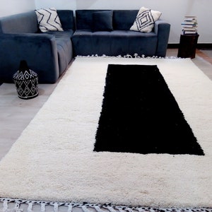 May include: A white shag rug with a black rectangular shape in the center. The rug has a fringe border.