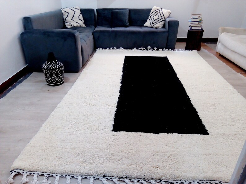 May include: A white shag rug with a black rectangular shape in the center. The rug has a fringe border.