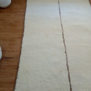 Puede incluir: Una alfombra blanca con una franja marr&oacute;n en el centro. La alfombra est&aacute; sobre un suelo de madera.
