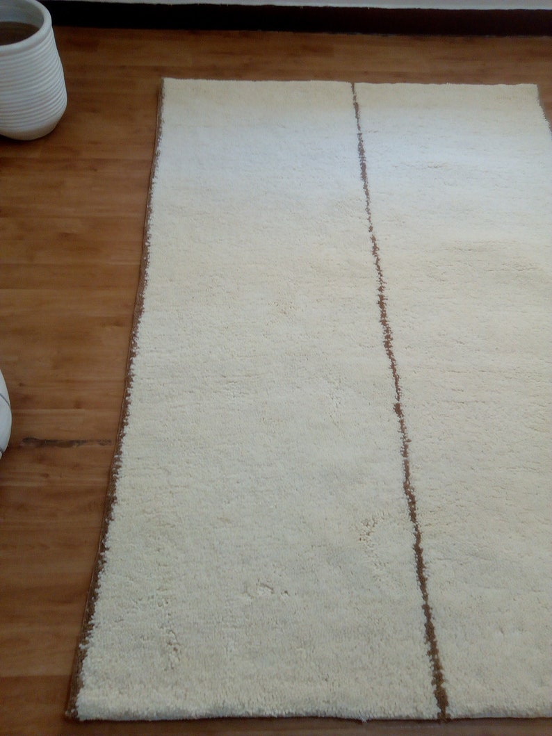 Puede incluir: Una alfombra blanca con una franja marr&oacute;n en el centro. La alfombra est&aacute; sobre un suelo de madera.
