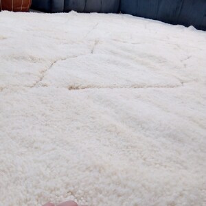 Puede incluir: Una alfombra de pelo blanco con un patr&oacute;n sutil. La alfombra es suave y esponjosa, y ser&iacute;a perfecta para una sala de estar o un dormitorio.