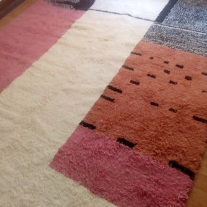 May include: A colorful geometric rug with a white background and pink, orange, and black stripes. The rug has a soft, fluffy texture.