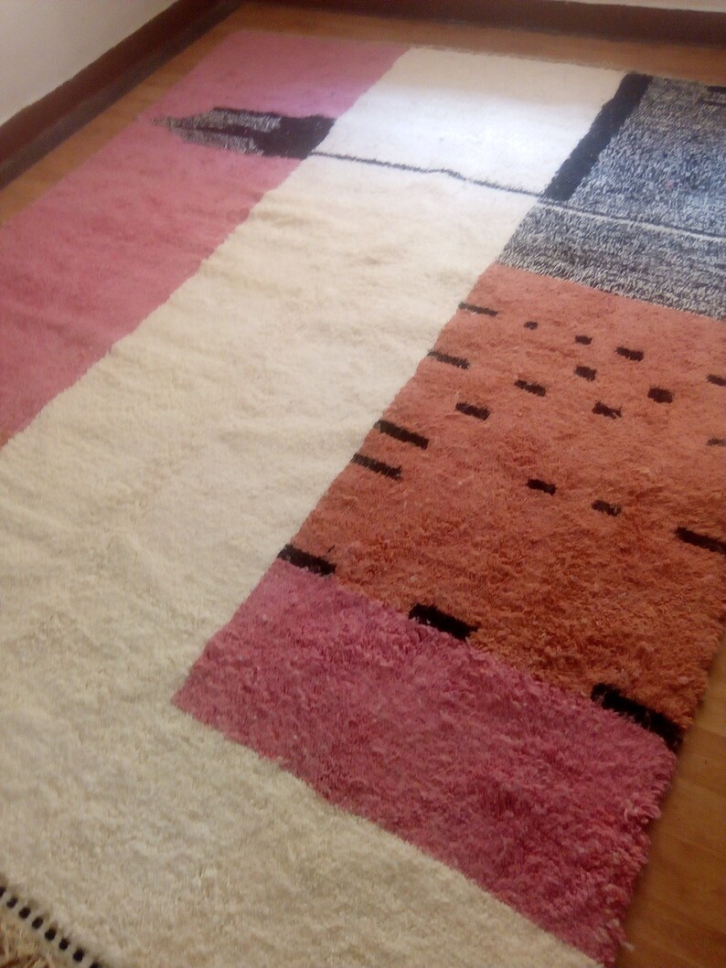 May include: A colorful geometric rug with a white background and pink, orange, and black stripes. The rug has a soft, fluffy texture.