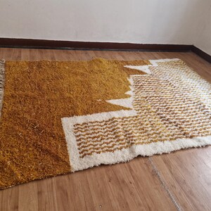 May include: A mustard yellow and white shag rug with a geometric pattern. The rug has a fringe border.