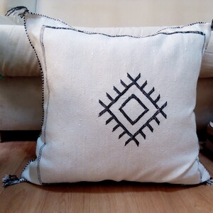 May include: White throw pillow with black embroidered geometric design. The pillow has black tassels on the corners.