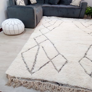 May include: A white shag rug with a geometric pattern in black. The rug has a fringe border and is laid out on a light wood floor.