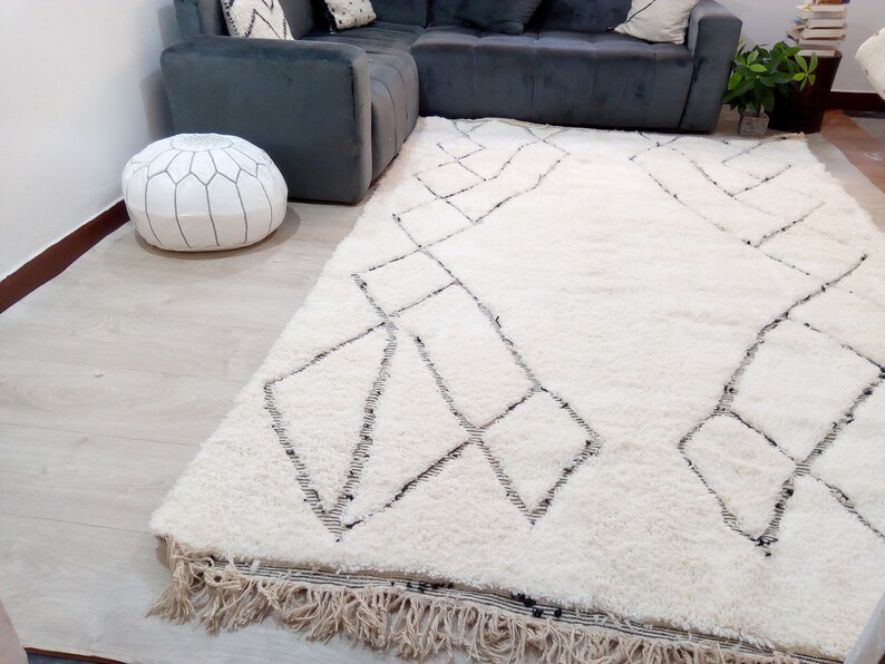 May include: A white shag rug with a geometric pattern in black. The rug has a fringe border and is laid out on a light wood floor.