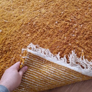 May include: A mustard yellow rug with a white fringe. The rug is folded in half, revealing a striped pattern on the underside.