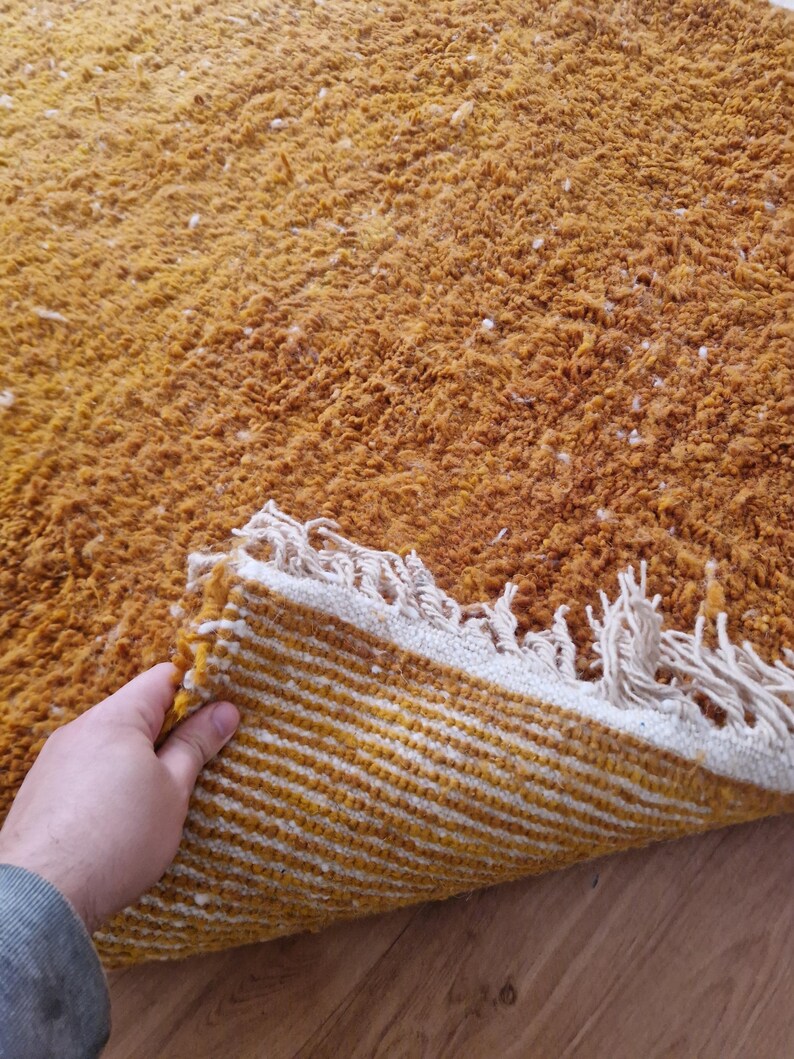May include: A mustard yellow rug with a white fringe. The rug is folded in half, revealing a striped pattern on the underside.